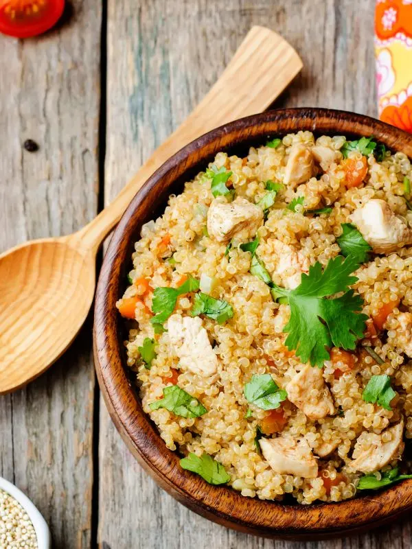 quinoa spanish rice with chicken in a clay bowl on a wooden table.