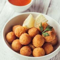 shrimp croquettes in a withe bowl, served with lemon and sauce.