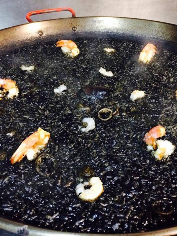 spanish black rice, or black paella in a paella pan with prawns and squid