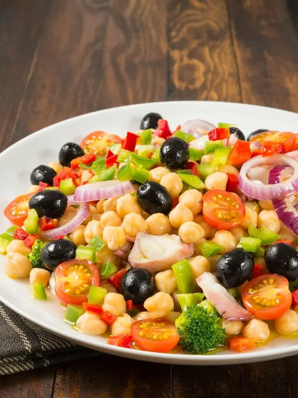 spanish chickpea salad with olives, onion, tomatoes and brocolli in a bowl on a wooden table
