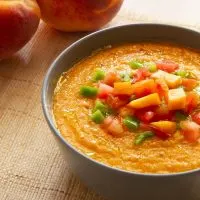 Peach And Tomato Gazpacho in a bowl with fresh peaches next to it.
