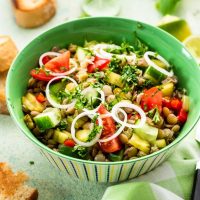 spanish lentil salad in a green bowl with toast next to it.