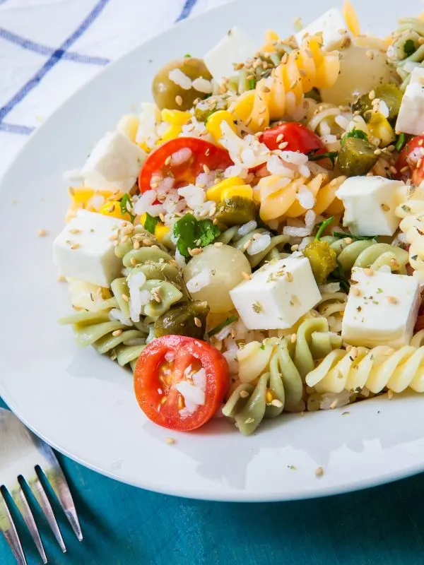 spanish macaroni salad with cheese, tomatoes and olives on a white plate.
