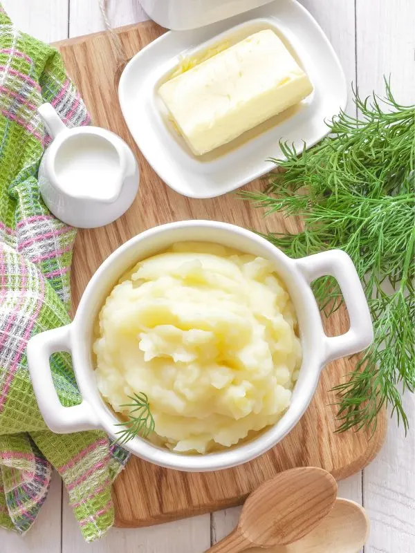 spanish mashed potatoes in a bowl, next to butter, cream and fresh dill.