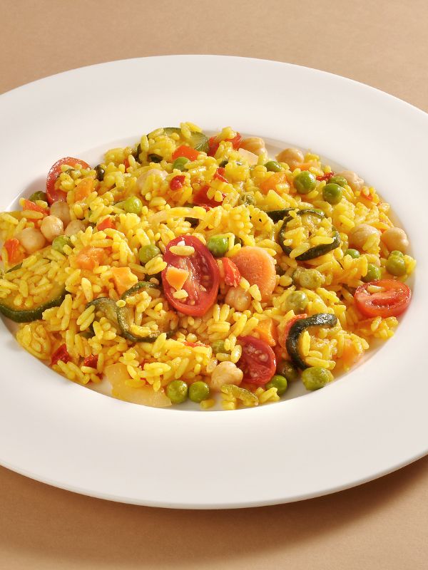 vegetable paella recipe with peas, tomatoes and peppers in a white plate.
