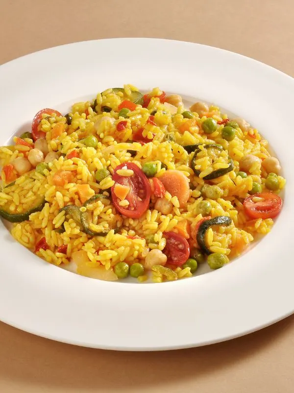 vegetable paella recipe with peas, tomatoes and peppers in a white plate.