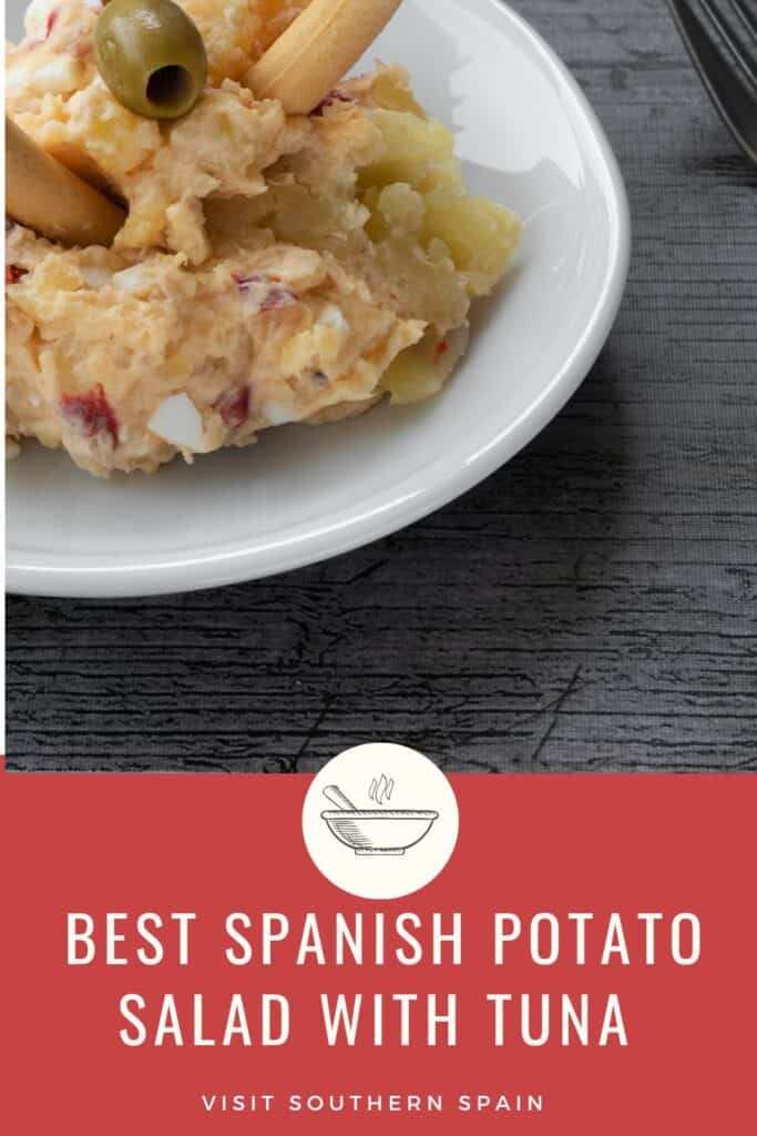 a pin with Spanish potato salad with tuna served on a white plate with bread sticks. 
