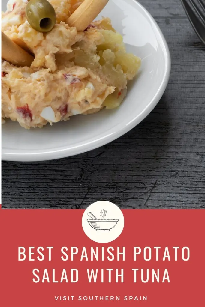 a pin with Spanish potato salad with tuna served on a white plate with bread sticks. 