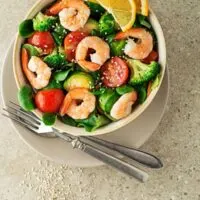 Ensalada de Broccoli with prawns in a bowl on a plate with spoon and fork