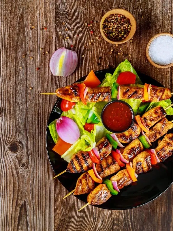 Spanish Chicken Skewers on a black plate served with sauce