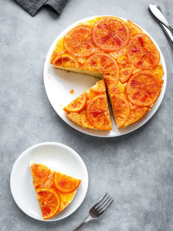 a spanish orange cake slice on a plate next to a whole cake - Heavenly Spanish Orange Cake Recipe