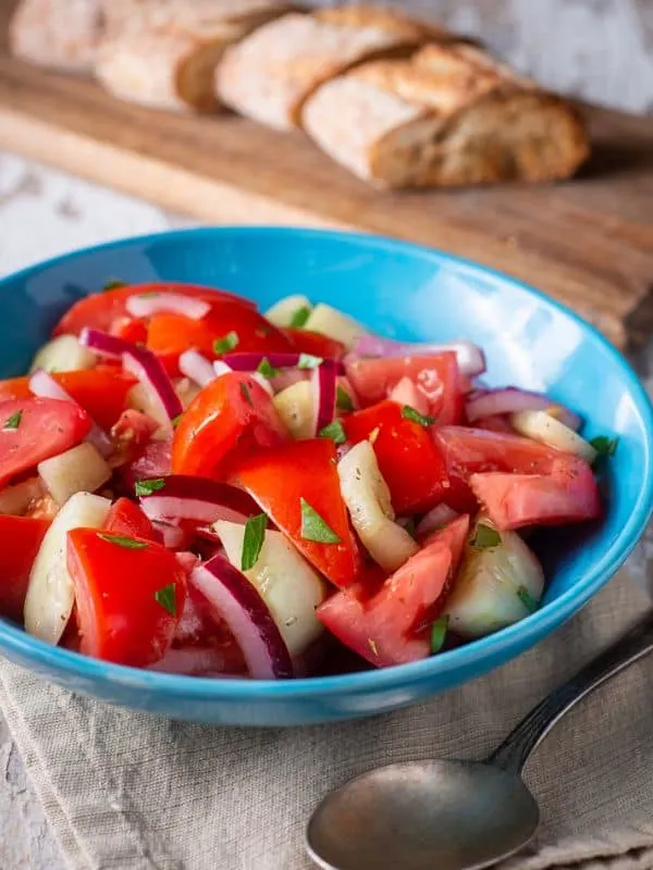 ensalada de pepino in a blue bowl with fresh bread in the background.
