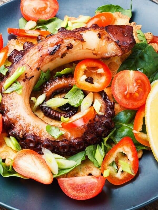 Spanish octopus salad recipe with tomatoes on a blue plate. 