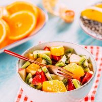 spanish fruit salad in a white bowl with slices of orange in the background.