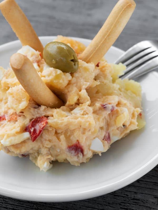 spanish potato salad with tuna served on a small plate with bread sticks and olive