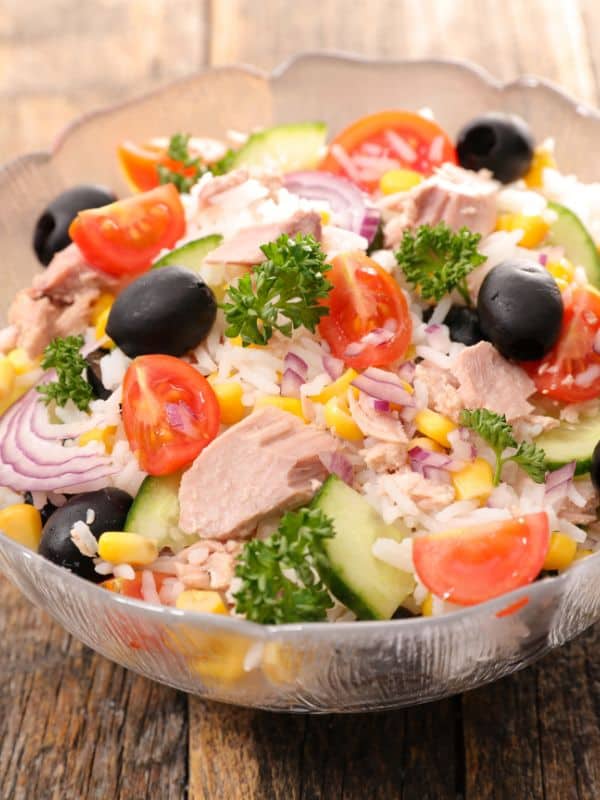 Spanish rice salad in a glass bowl with olives, tomatoes and onion.