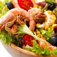 closeup of a ensalada de gambas with tomatoes, olives and lettuce in a wooden bowl