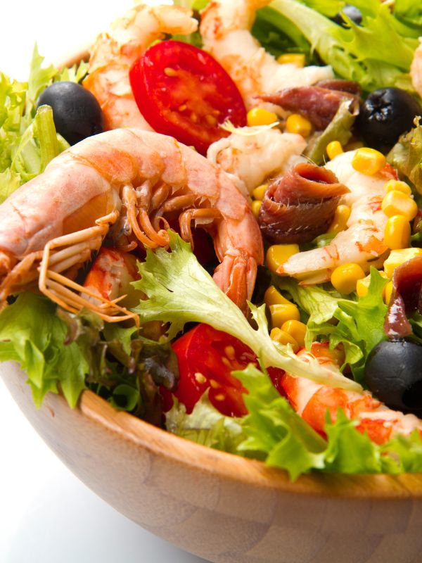 closeup of a ensalada de gambas with tomatoes olives and lettuce in a wooden bowl - Best Ensalada de Gambas Recipe [Shrimp Salad]