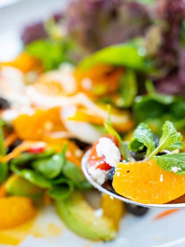 closeup of a spoon with traditional spanish salad with oranges, cod and other fresh vegetables.