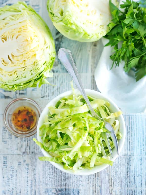ensalada de repollo in a bowl with a slices cabbage next it and paprika. - Best Ensalada de Repollo Recipe [Spanish Cabbage Salad]