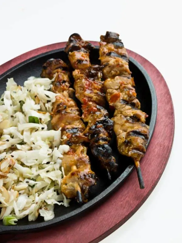 skewers with a side of ensalada de repollo on a black plate.
