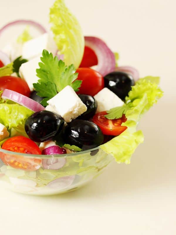 spanish summer salad with olives, onion and tomatoes in a glass bowl.