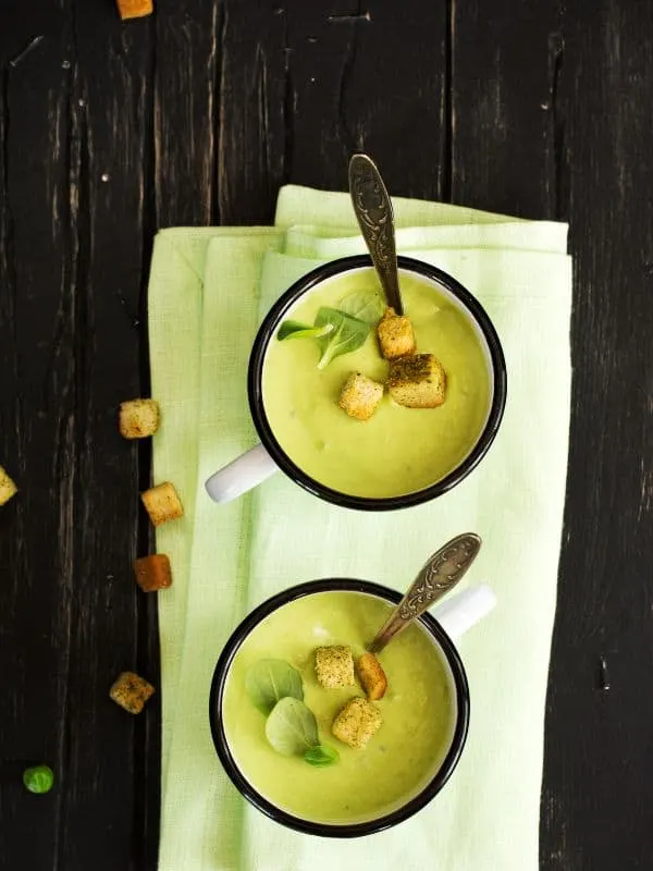 2 cups of pea gazpacho on a black surface.