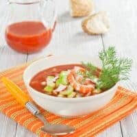 seafood gazpacho in a bowl with fresh vegetables on top and served on a table cloth