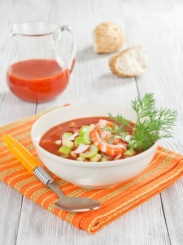 seafood gazpacho in a bowl with fresh vegetables on top and served on a table cloth