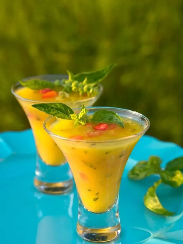 Gazpacho de mango in 2 serving glasses on a blue surface