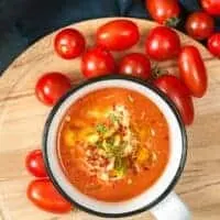 Tomato Soup With Coconut Milk in a bowl on a wooden board with tomatoes next to it.