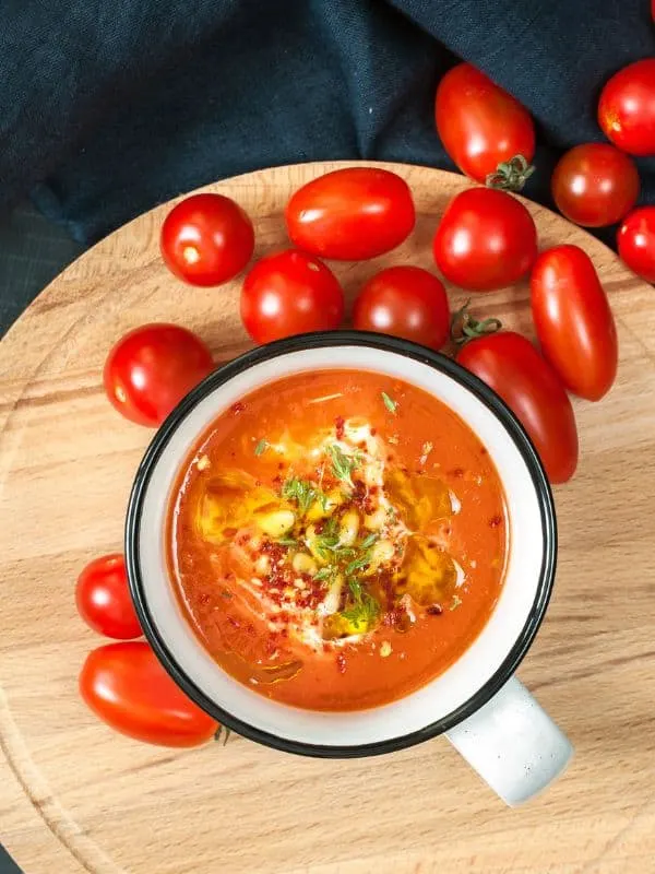 tomato juice gazpacho in a bowl on a wooden board with tomatoes next to it.