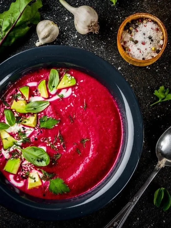 beetroot gazpacho served in a black bowl decorated with fresh vegetables. 