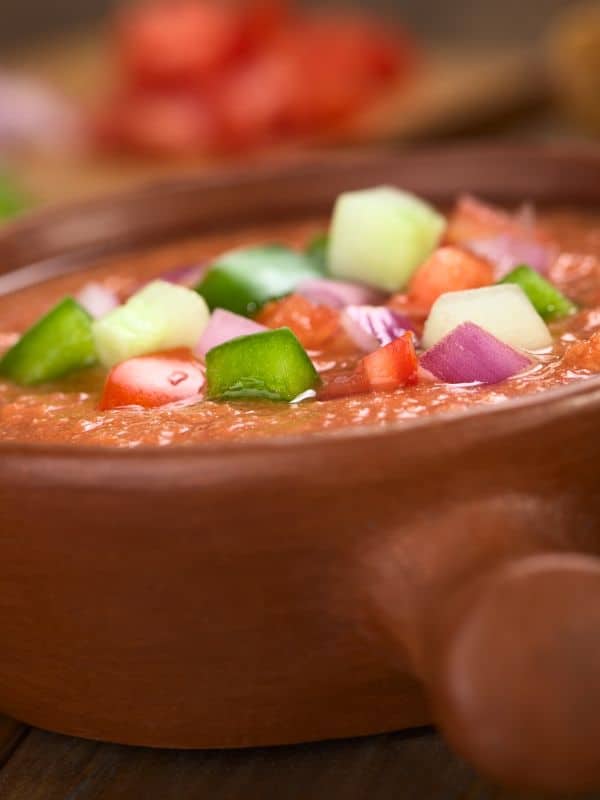 closeup with cold vegetable soup in a clay pot decorated with fresh vegetables - Spanish Cold Vegetable Soup Recipe