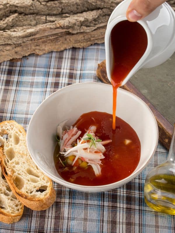 cold shrimp soup in a bowl served with 2 slices of bread on a rustic table