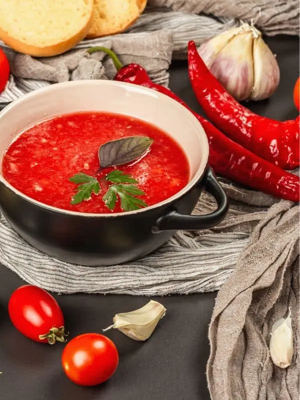 spanish spicy gazpacho in a bowl with tomatoes bread and spicy peppers next to it. - Best Spicy Gazpacho Recipe from Spain