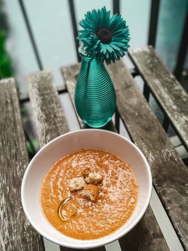 sweet corn gazpacho in a bowl on a wooden table with a flower next to it - Easy Sweet Corn Gazpacho Recipe