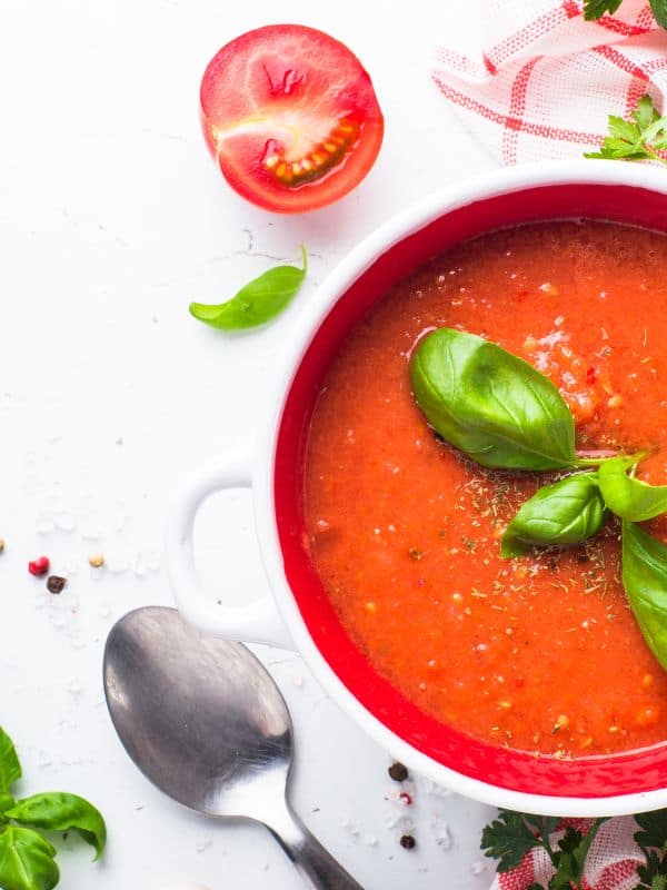 avocado tomato soup in a bowl with half of tomato next to it and decorated with basil
