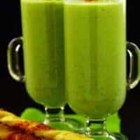 2 tall glasses of pea gazpacho with bread sticks next to it with back background