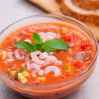 a glass bowl with seafood gazpacho served with slices of bread