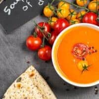cherry tomato soup in a bowl with cherry tomatoes and bread next to it.