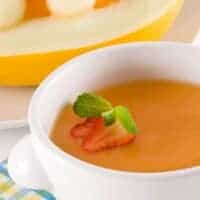 chilled melon soup decorated with 2 slices of strawberry and a melon in the back