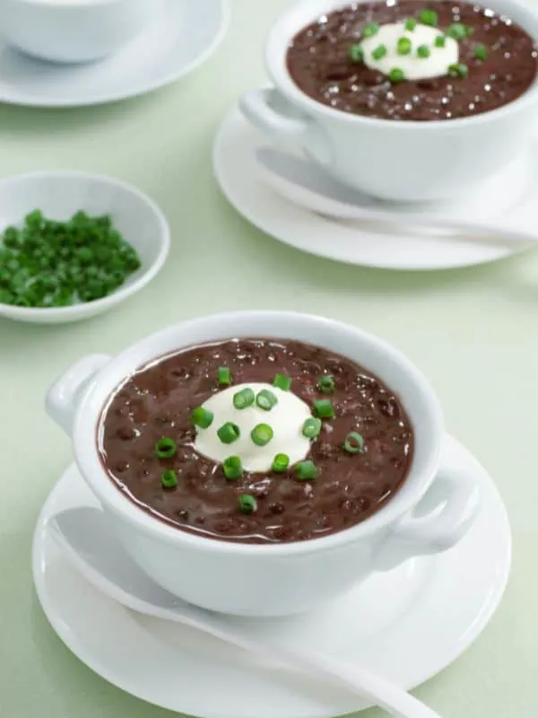 cold bean soup in 2 white bowls decorated with cream and spring onion