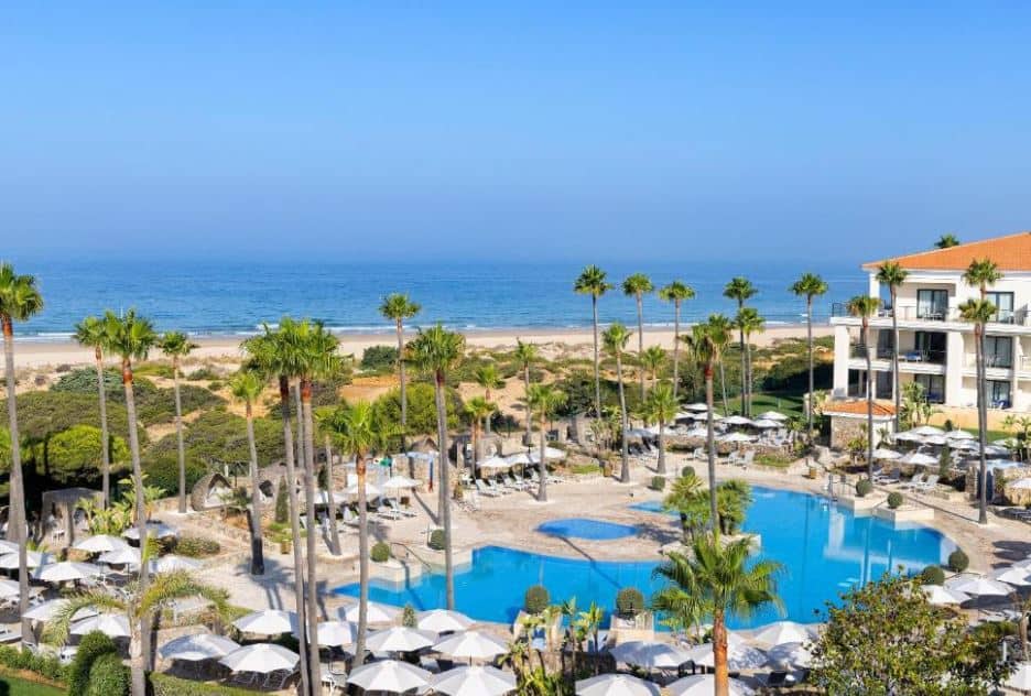 pool area with sun lounges and palm trees, next to the beach at Hipotels Barrosa Palace & Spa, luxury hotels in Andalucia