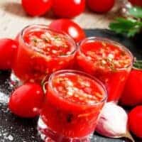 tomato juice gazpacho in 3 glasses with garlic and fresh tomatoes around them