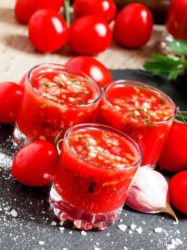 tomato juice gazpacho in 3 glasses with garlic and fresh tomatoes around them