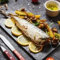 Spanish Baked Mackerel Recipe on a black plate with potatoes and lemon slices