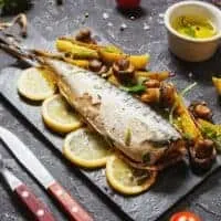 Spanish Mackerel oven Recipe on a black plate with potatoes and lemon slices