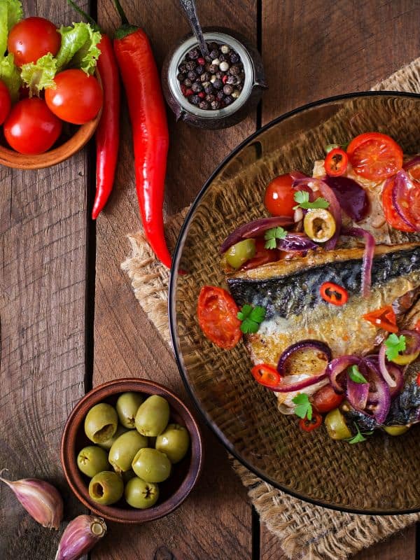 Mediterranean Mackerel recipe on a glass plate with other ingredients next to it.