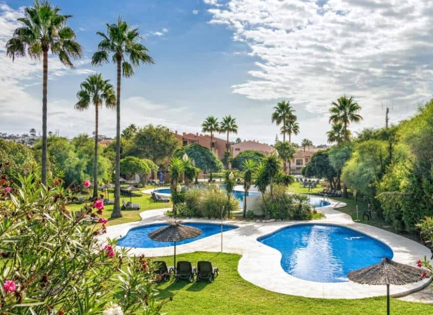 garden with pool areas, palm trees and sitting areas at Los Amigos Beach Club, one of the best family resorts in malaga